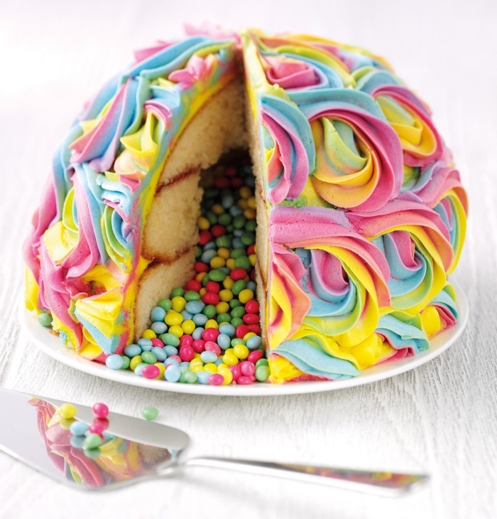 gateau-a-la-vanille-aux-smarties-forme-dôme-glaçage-arc-en-ciel-à-la-poche-à-douille recette de gateau a la vanille en forme de dôme, au glaçage de roses arc-en-ciel, rempli de bonbons multicolores