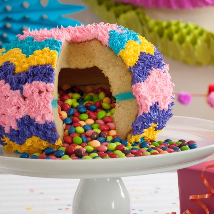 pinata cake en forme de sphère avec un centre creux rempli de bonbons, au glaçage coloré réalisé à la poche à douille décorative