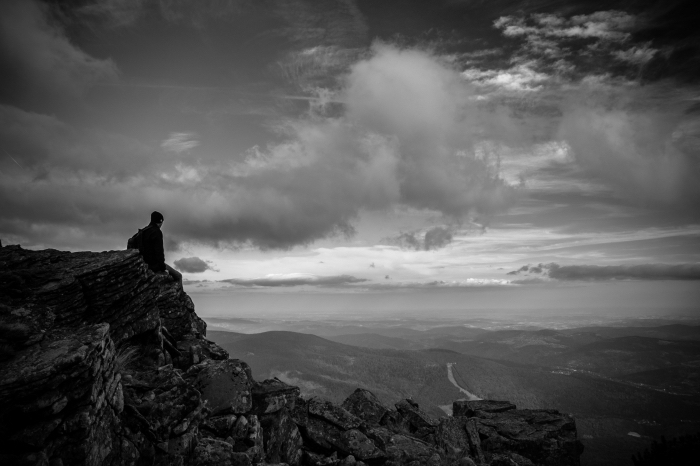 belle photo d'homme assis sur un rocher contemplant la nature sous le spectacle des nuages, portrait noir et blanc l'homme et la montagne