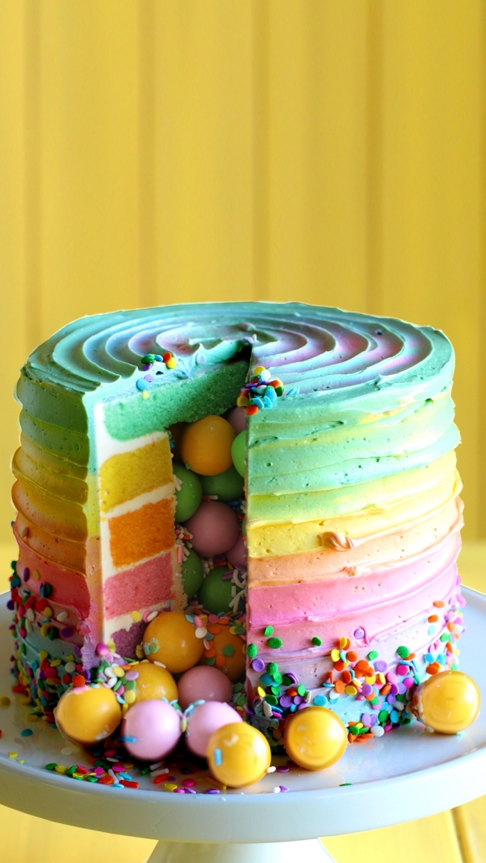 gateau arc en ciel haut en couleur rempli de bonbons, au glaçage coloré qui reprend les couleurs de l'intérieur