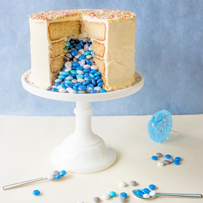gateau pinata à la vanille pour rempli de bonbons bleus pour annoncer le sexe du futur bébé, gâteau à couches au glaçage au beurre posé sur un présentoir à gâteau