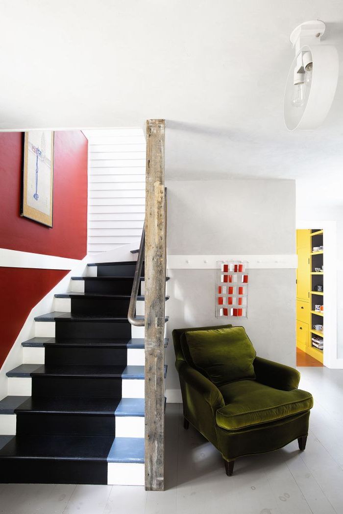 relooker un escalier un bois à l'aide de la peinture, une large bande de peinture noire qui parcourt l'escalier pour un effet tapis d'escalier, en contraste avec le blanc et le rouge qui domine la cage d'escalier