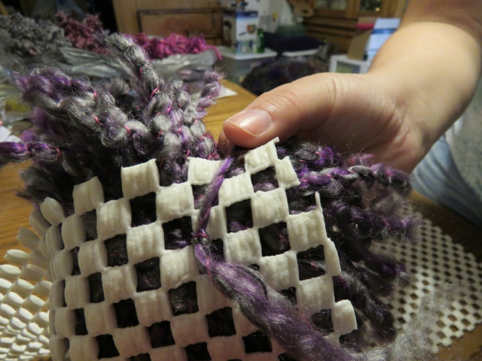 le dos d'une toile canevas, noeud avec les fils en laine de grands pompons pourpres, diy tapis laine