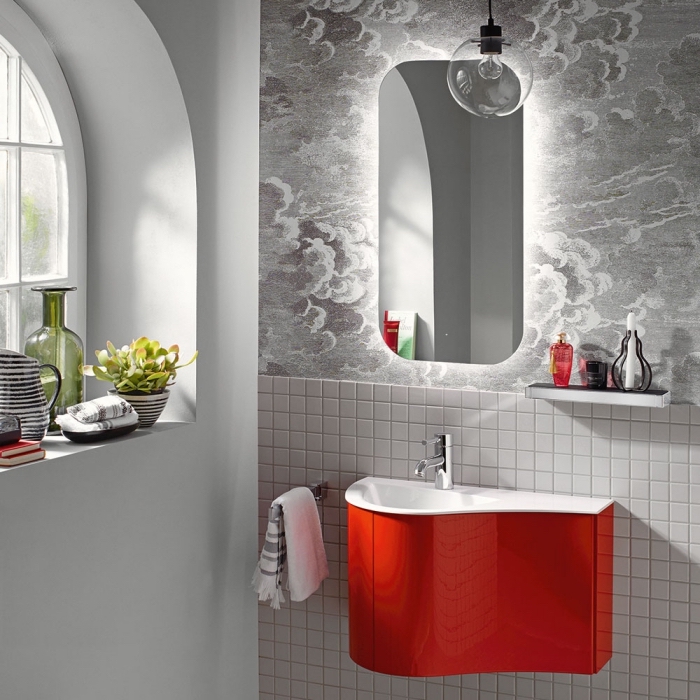 un meuble sous vasque suspendu à finition rouge en contraste avec le revêtement en papier peint et carrelage mural de mosaïque blanc et e