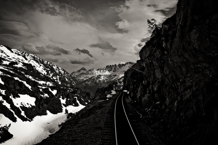 photographie noir et blanc de chemin de fer dans la montagne hivernal qui se faufile entre les rochers