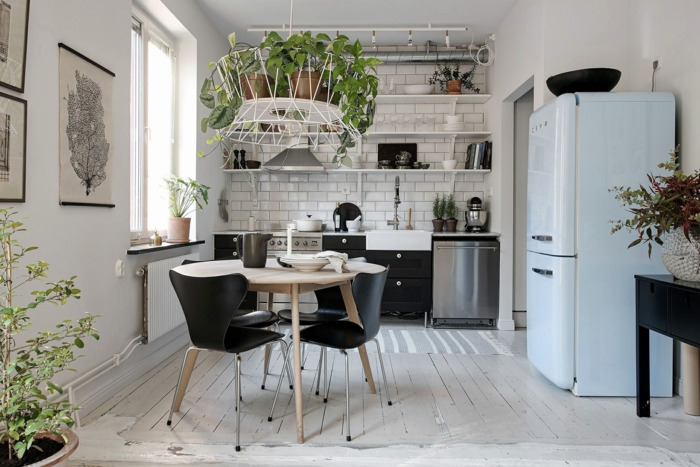 petite cuisine blanche, table ronde avec des chaises noires, parquet blanchi, réfrigérateur bleu pastel, étagères, carreaux métro, plusieurs plantes