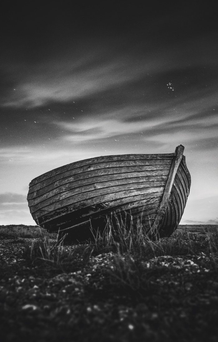 image noir et blanc poétique d'une barque solitaire abandonnée sur la rive sous les nuages dansant