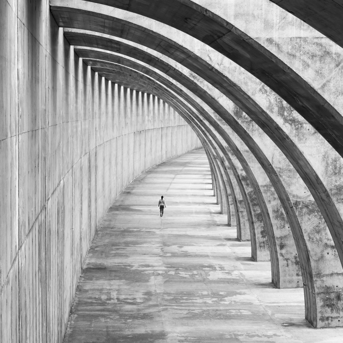 photo noir et blanc femme marchant sous un arc en béton, photo originale d'un bâtiment moderne