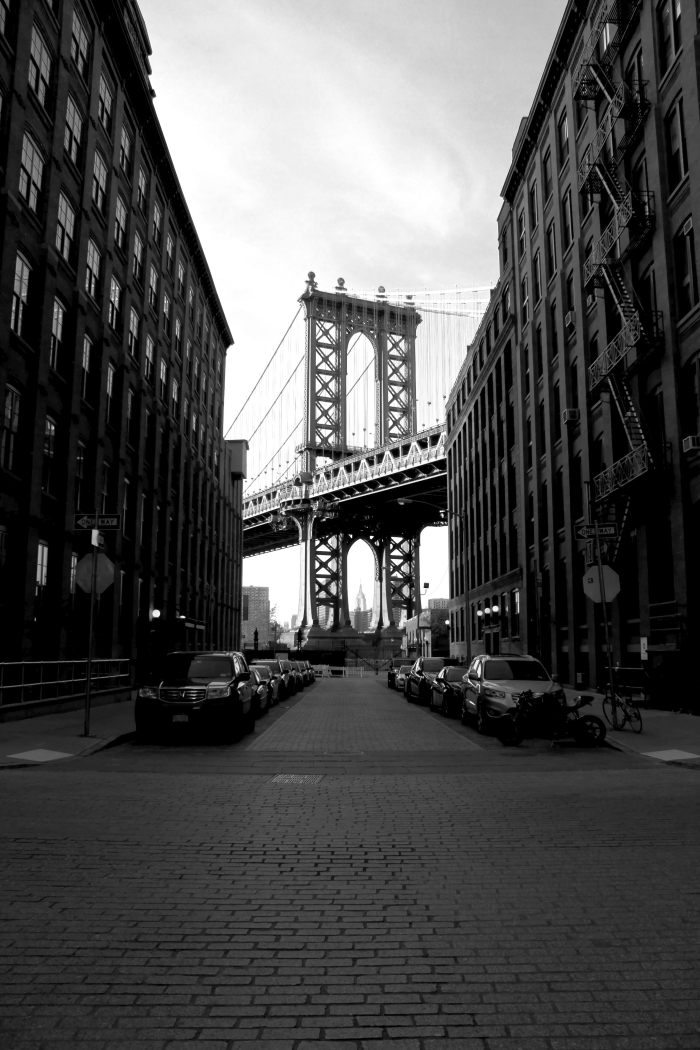vue sur une partie du pont de new york entre de grands bâtiments, paysage urbain en noir et blanc pris d'une perspective originale