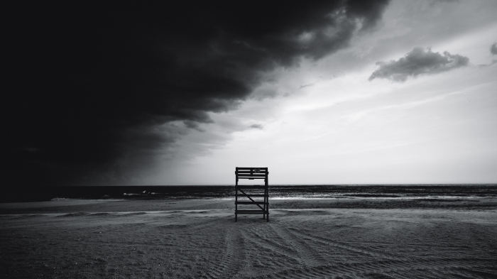 paysage marin en noir et blanc d'un plage déserte avec un poste de surveillance solitaire et un ciel orageux à demi couvert de nuages