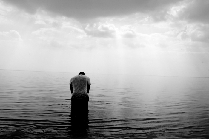 portrait noir et blanc le jeune homme et la mer, un homme la tête baissée, accroupi dos au rivage