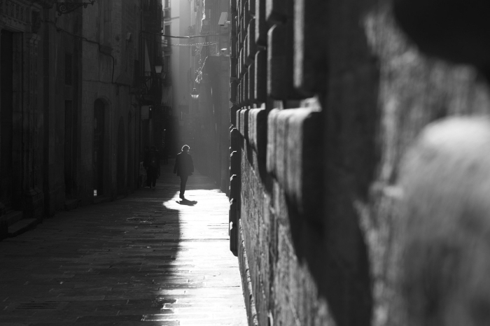 photographie noir et blanc de rue homme marchant dans une ruelle étroite et la lumière tombant sur une partie du pavement