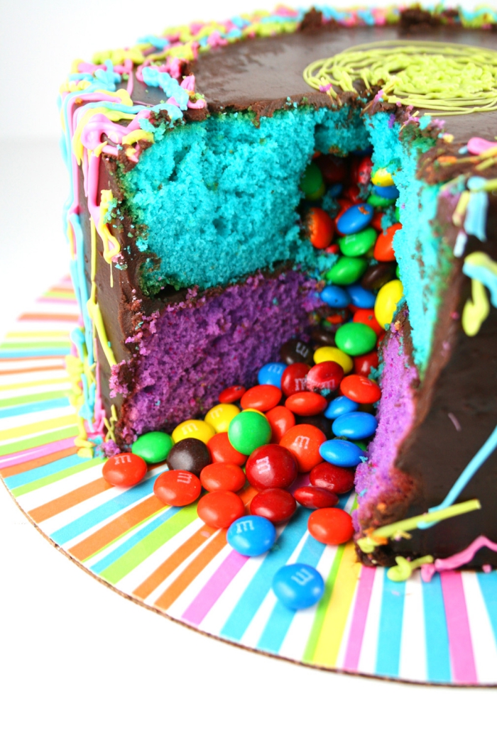 recette-gateau-anniversaire-chocolat-génoises-de-couleur-surprise-smarties-présentoir-rayures-colorées idée de gâteau d'anniversaire fait-maison, gateau smarties recouvert de ganache composé de deux couches de génoise de couleur bleu et violet qui renferme des bonbons