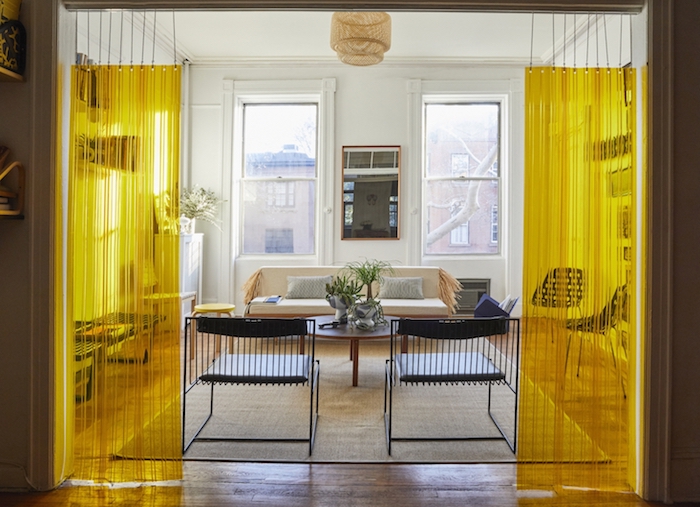 cloison decorative rideau plastique jaune suspendu, canapé beige, chaises metalliques noires, table basse ronde