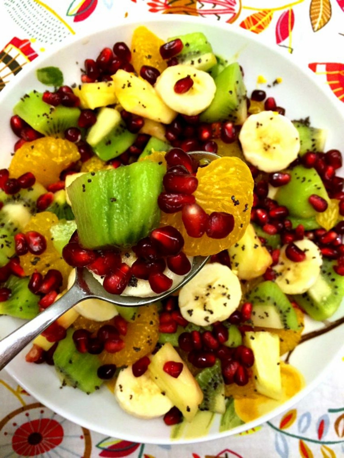 salade fraîche riche en vitamines, kiwi, grenade, bananes, graines de pavot, assiette blanche, nappe aux dessins