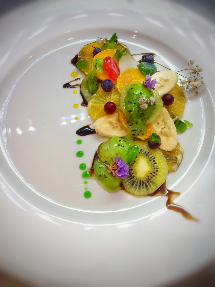 joli arrangement de fruits sur assiette de présentation, gouttes de sirop vert, kiwis tranchés, baies bleues, kiwis, groseilles à maquereau 