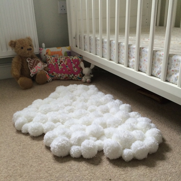 jolie décoration pour la chambre d'enfant, petit tapis blanc forme irrégulière, ourson peluche, coussin mignon et jouets sous le lit de bébé