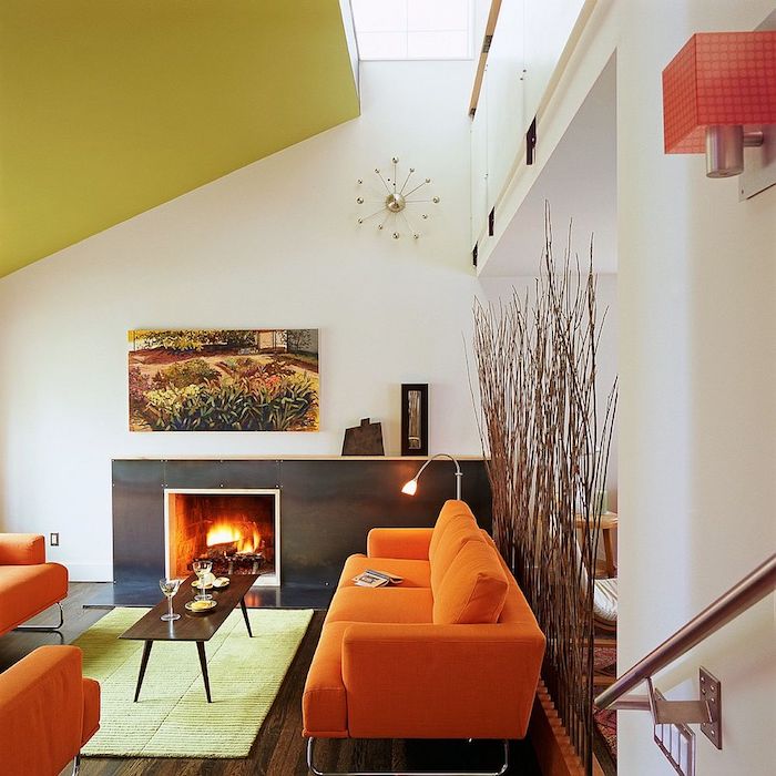 amenagement salon sous pente avec fauteuils et canapé orange, cheminée moderne, table basse bois, parquet marron foncé, separation branches de bois