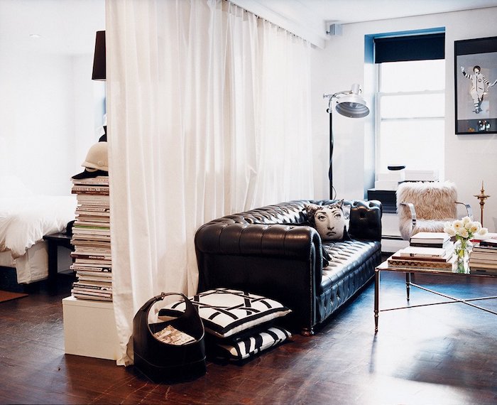 rideau blanc semi transparent pour séparer un salon avec canapé noir, deco graphique, piles de livres, parquet bois foncé