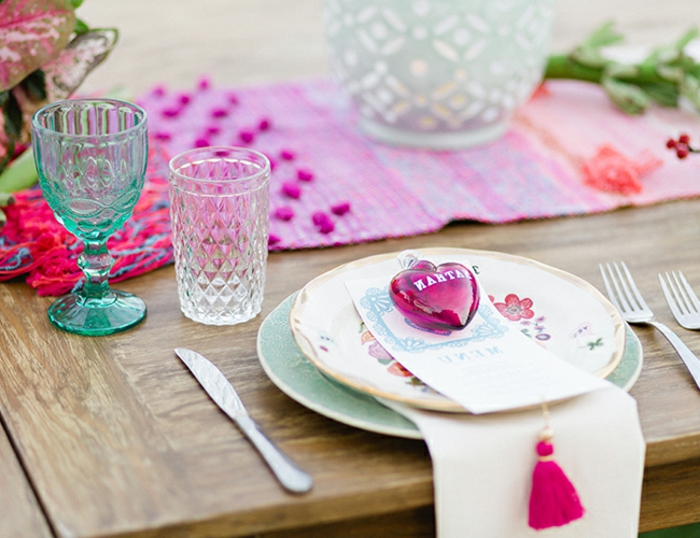 table en bois, sous assiette bleue, assiette blanche, verres en verre, chemin de table tissu, bougeoirs en verre, coeur rose, frange rose