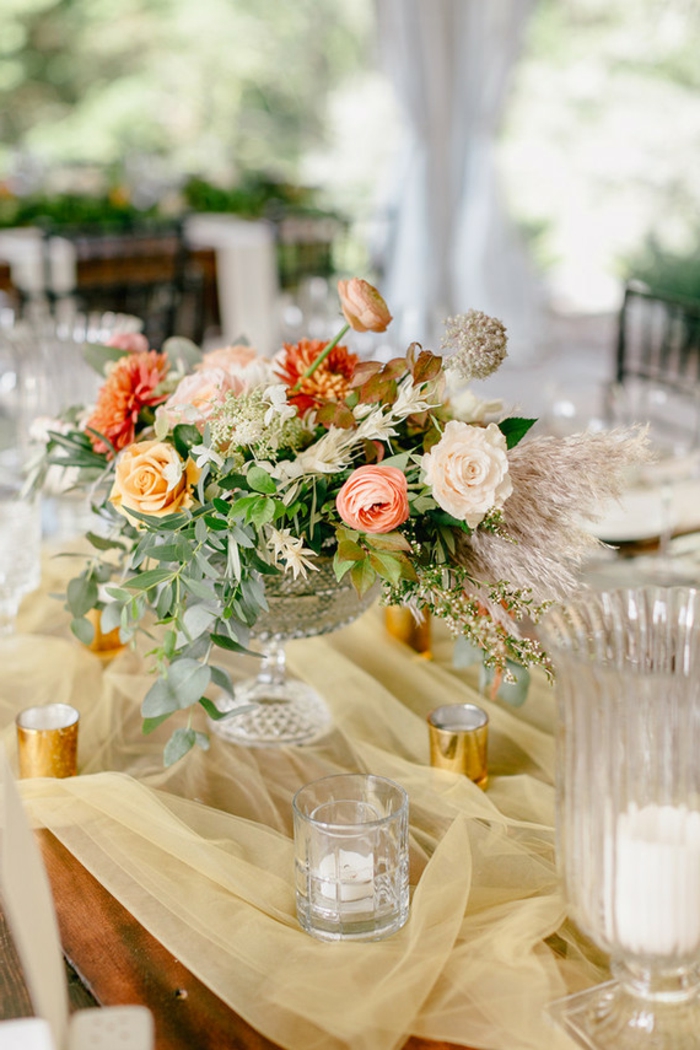 chemin de table tissu fin couleur crème, grand bol avec bouquet de fleurs, verres en verre, porte-bougies dorés