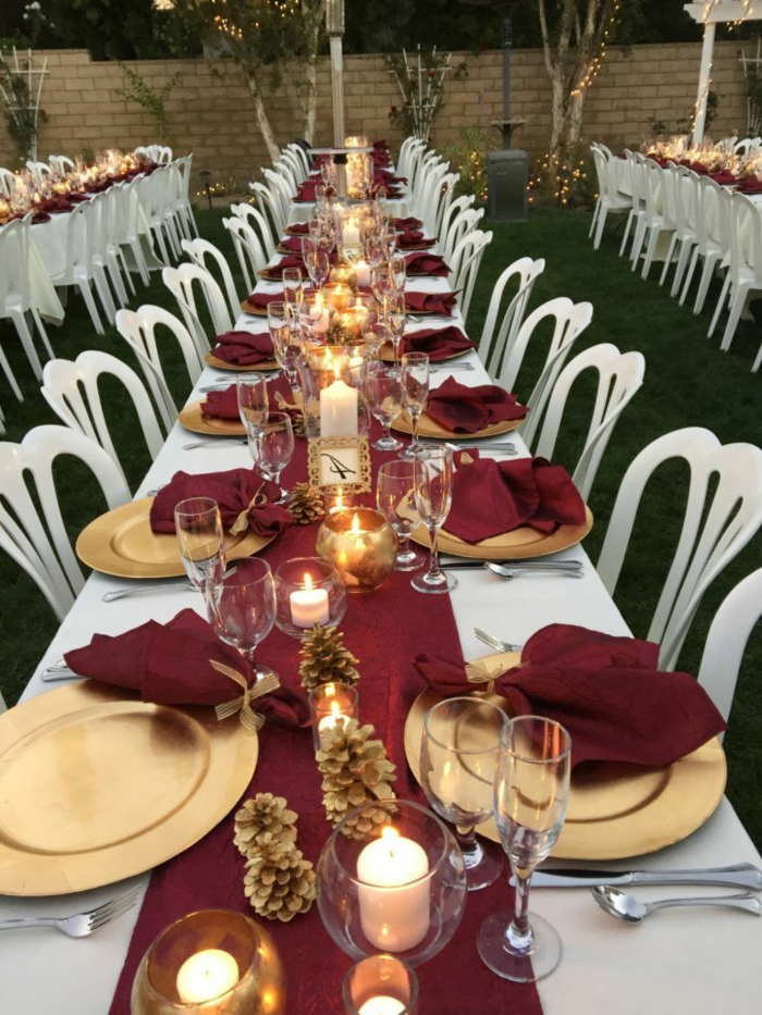 mariage à l'extérieur, chemin de table rouge, assiettes dorées plates, pommes de pin, serviettes rouges, nappe blanche