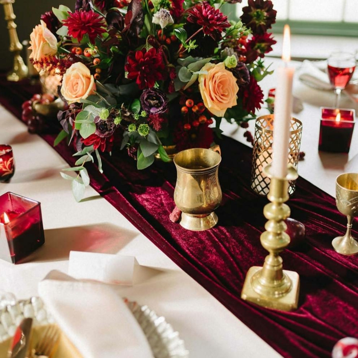 chemin de table rouge en velours, grand bouquet de roses et dahlias, porte bougie dorée et bougies rouges, table blanche