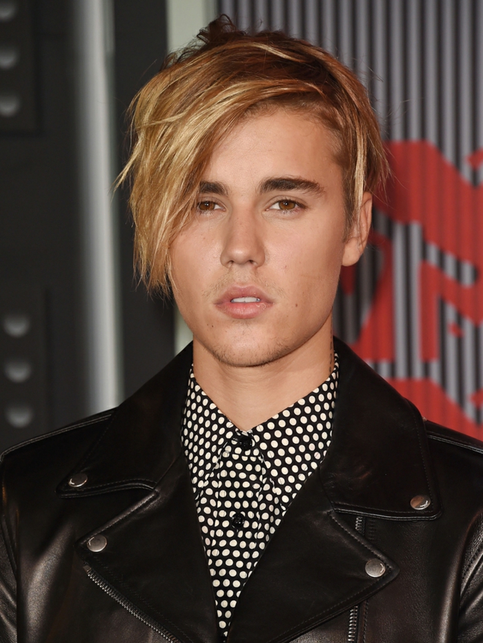 Justin Bieber avec un coupe moderne, cheveux blonds, frange sur le côté, chemise pointillé, veste noire