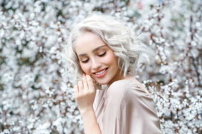 coloration blond polaire sur cheveux ondulés, blouse femme beige, idée de coiffure à effet décoiffé, maquillage nude
