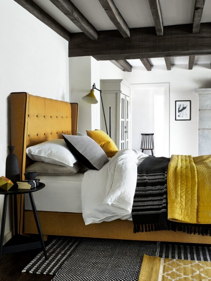 déco de chambre cozy aux murs blancs et plancher noir avec grand lit de couleur jaune moutarde, modèle plaid bohème chic noir avec frange