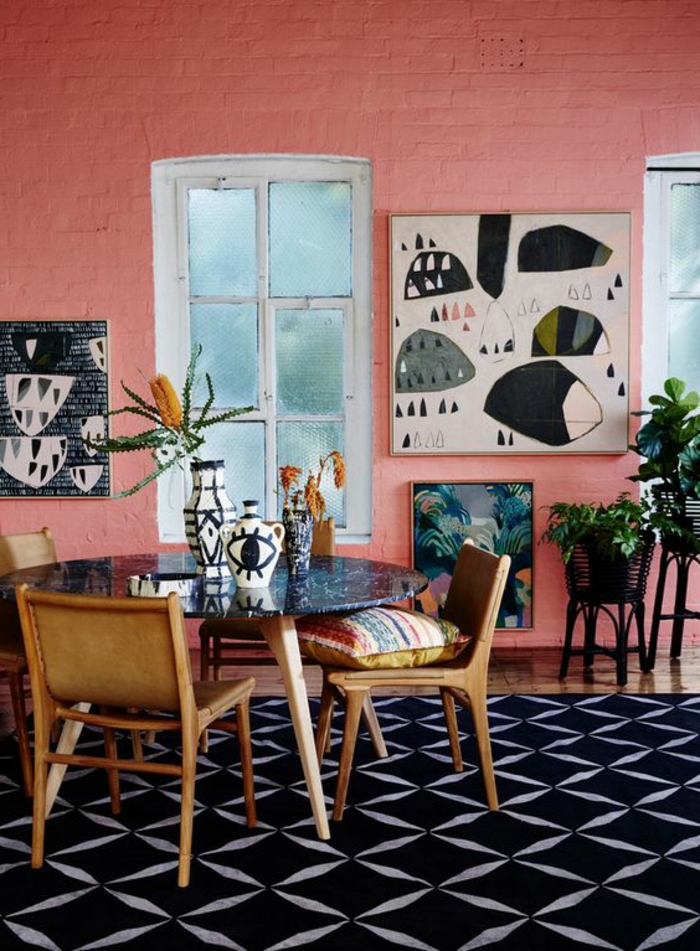 tapis noir motif géométrique, chaises vintage en bois autour d'une table ronde marbrée, plantes vertes, mur en briques peint en couleur saumon