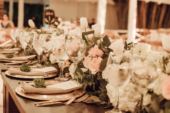petites succulentes posées sur les assiettes plates, ustensiles cuivrées, chemin de table en roses et fleurs blanches