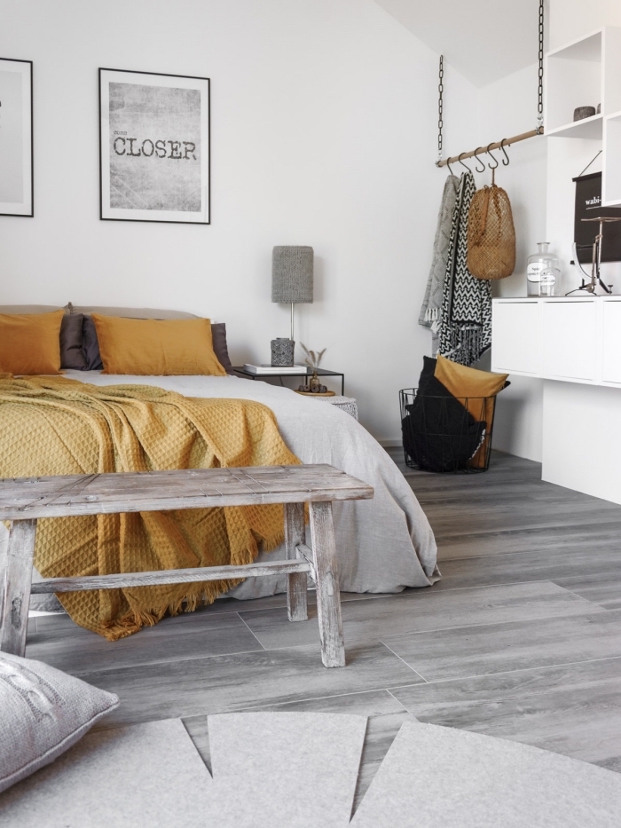 chambre à coucher de style minimaliste aux murs blancs et parquet gris clair, linge de lit et coussins décoratifs de couleur jaune moutarde