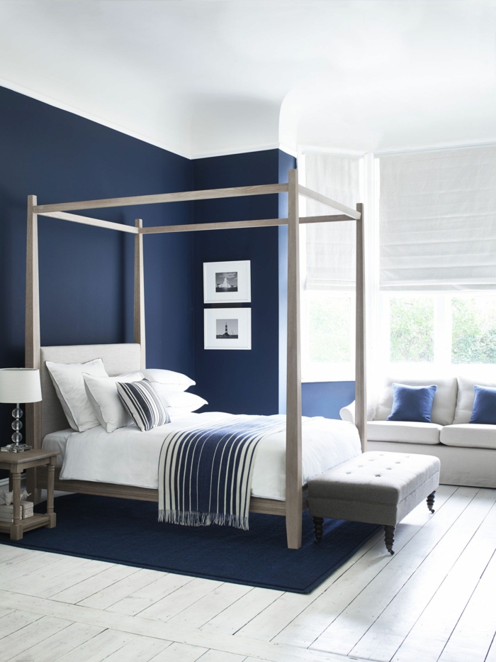 chambre en bleu et blanc, lit baldaquin, tabouret gris, sol en planches de bois, sofa blanc, coussins bleus