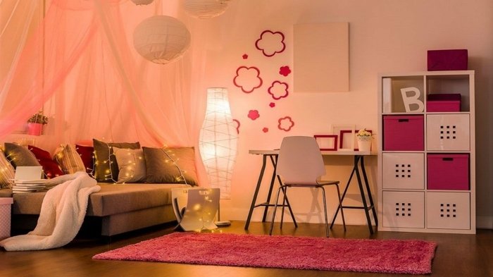 chambre d'enfant couleur pêche, tapis rose, plafonniers en papier, étagère en blanc et rose, petit bureau, guirlande lumineuse