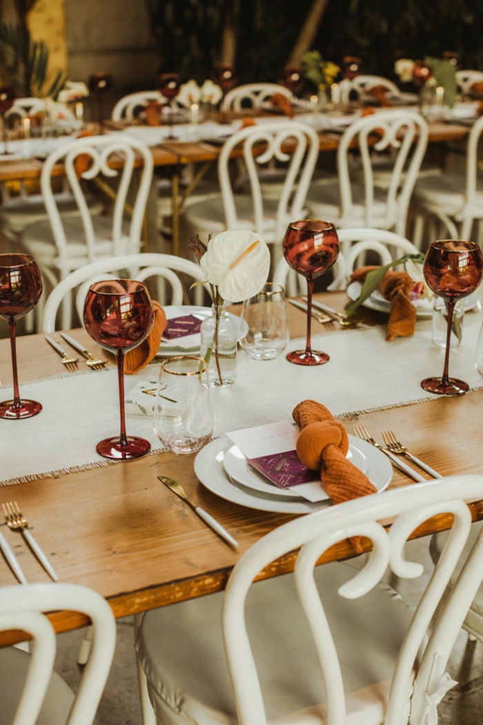 jolie table de mariage, flûtes à champagne, assiettes et sous-assiettes, serviette de table en noeud orange, chaises élégantes blanches