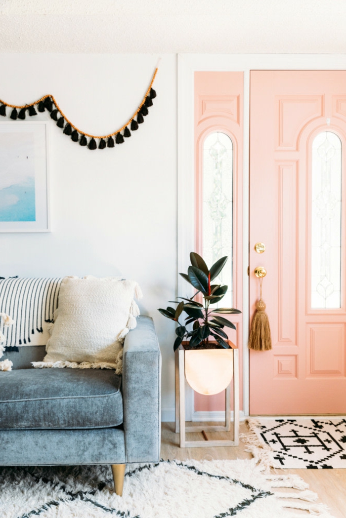 grande porte couleur corail, table de chevet pliante, plante décorative, guirlande de franges suspendue au mur, sofa bleu