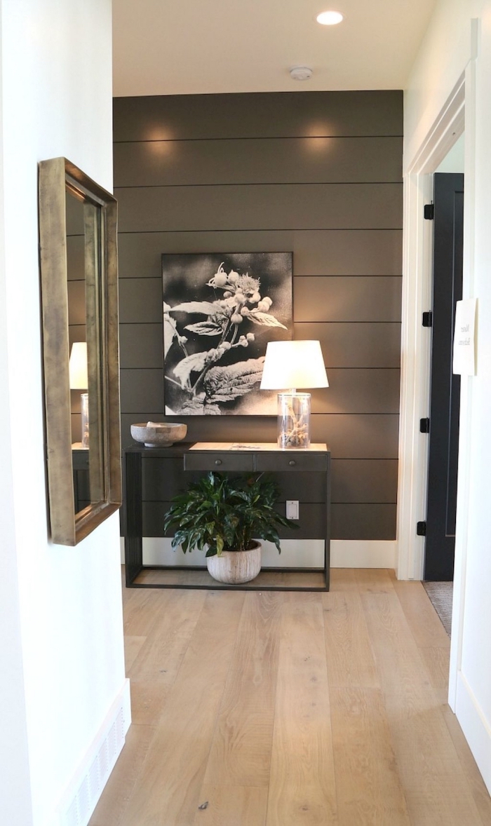 petit couloir blanc dans un appartement moderne dont le mur au fond revêtu de planches bois a été peint marron foncé