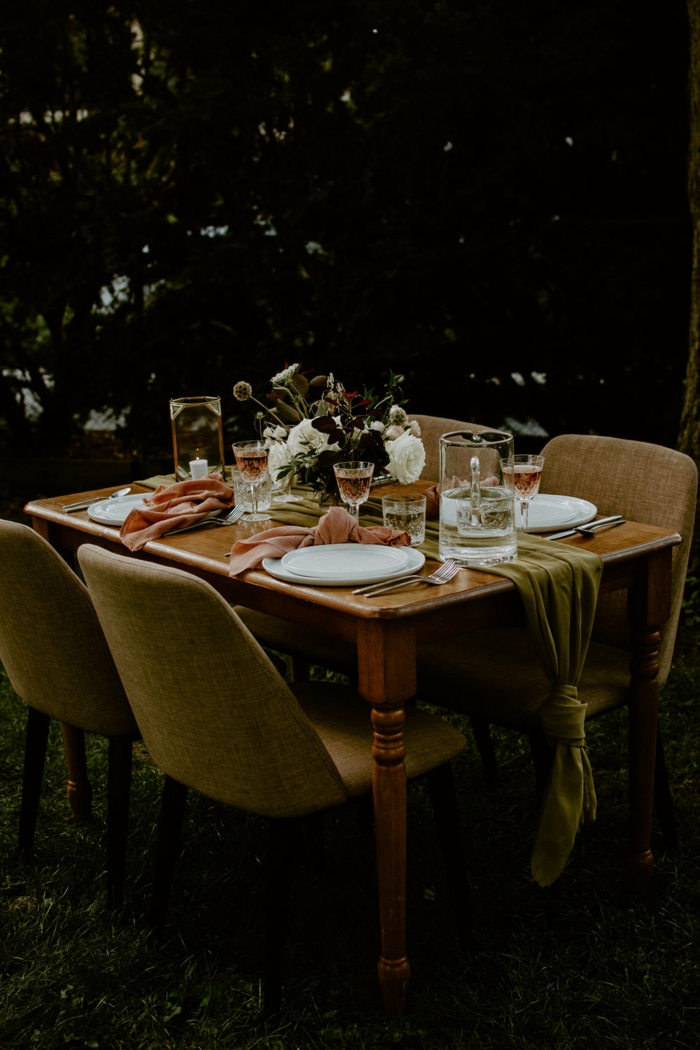 table de bois avec un chemin de table vert en tissu, assiettes blanches, serviettes de table roses, bouquet de fleurs blanches