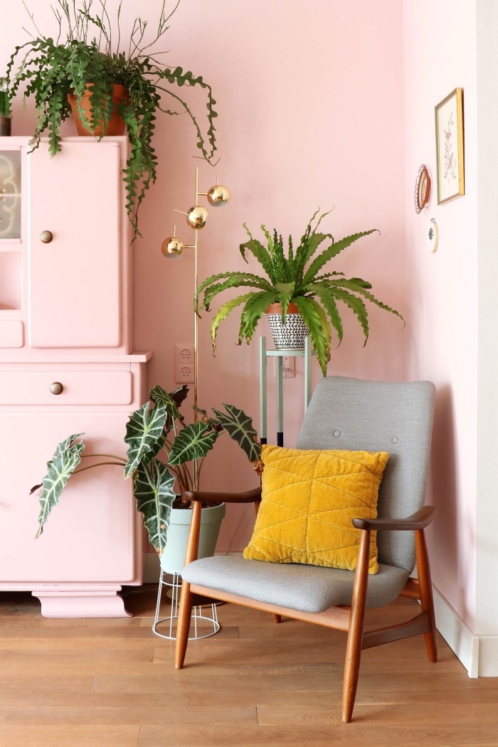 design intérieur féminin dans un salon aux murs rose pastel et parquet bois, modèle chaise fauteuil bois foncé décoré de coussin couleur moutarde