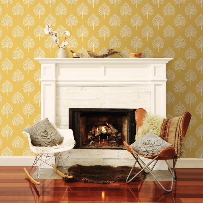 salon cozy avec cheminée blanche, modèle de papier peint de couleur moutarde avec dessins arbres, tapis faux fur marron imitation peau animale