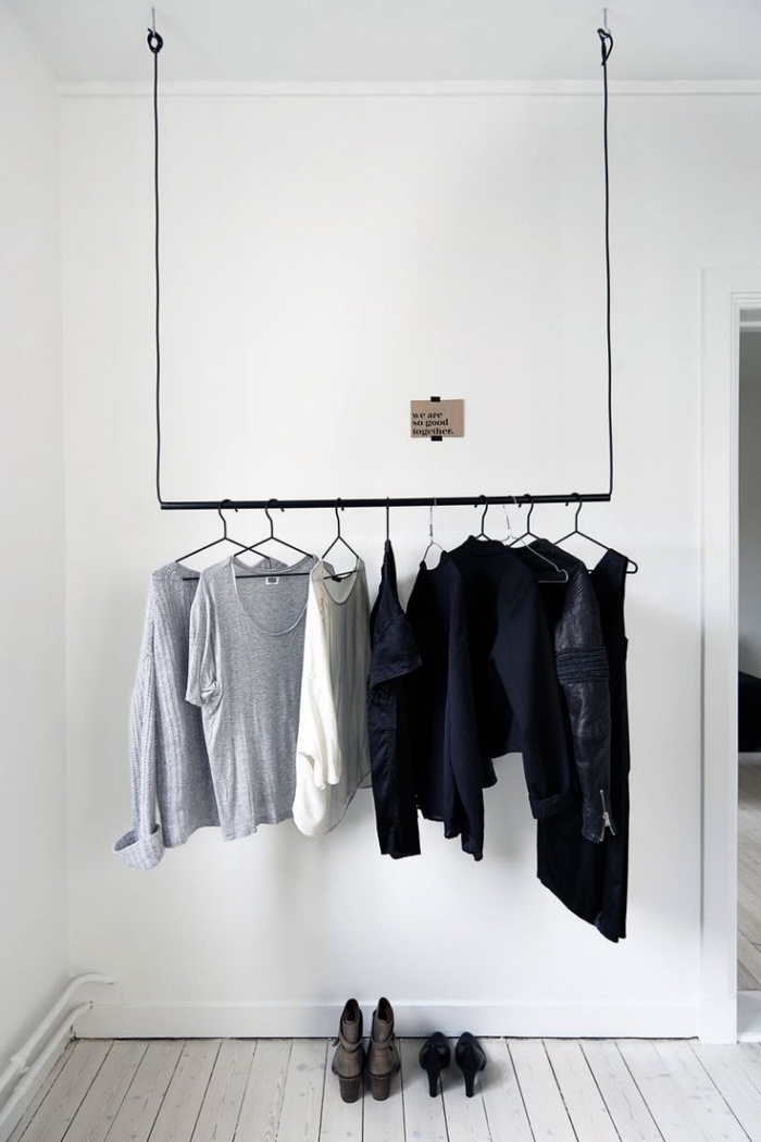 penderie ouverte minimaliste avec une barre en acier noir suspendue au plafond qui accueille quelques blouses et robes