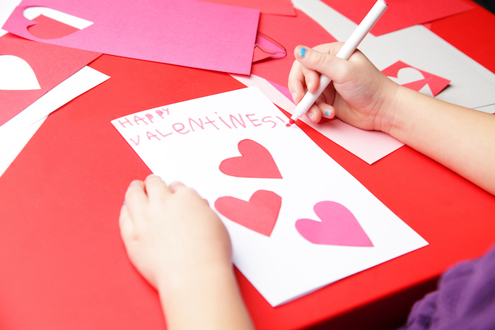activité manuelle primaire, carte de saint valentin dans papier blanc avec des coeurs en papier collés dessus et texte d amour
