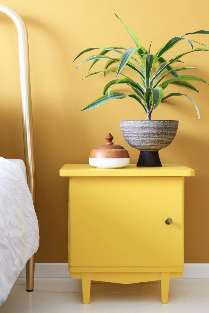 meuble de chevet moderne de couleur ocre, accessoires déco boîte à bijoux blanc et bois, chambre aux murs jaune et plancher blanc