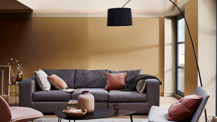 mur couleur marron, sofa gris, coussins terracotta, table basse asymétrique, chaises élégantes, grand lampadaire noir