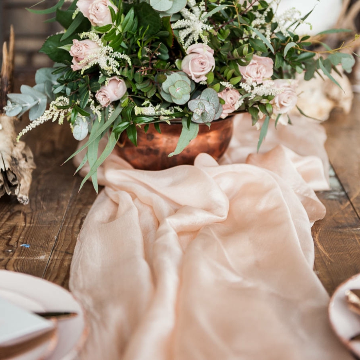 grand bol couleur cuivré avec bouquet de roses et feuillage, chemin de table rose, table en bois brut