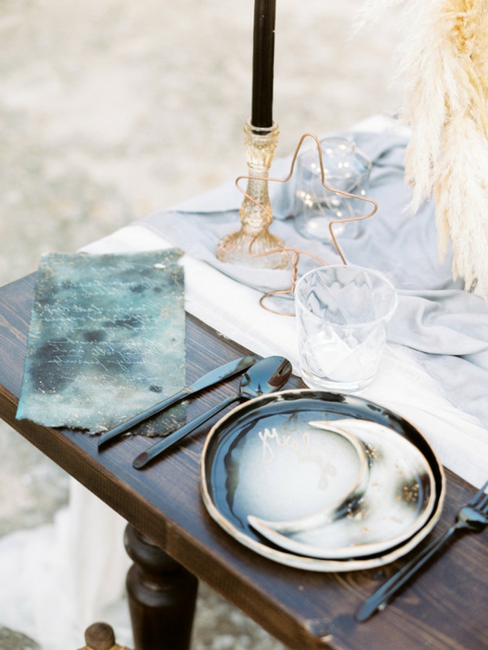table en bois foncé, assiettes artisanales, bougeoirs en cristal jaune, bougie noire, ustensiles noires