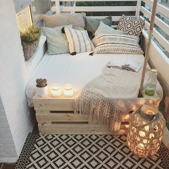 petit canapé lit en bois de palette avec matelas et coussins decoratifs gris et beige, tapis gris et noir, bougeoirs et bougies deco balcon