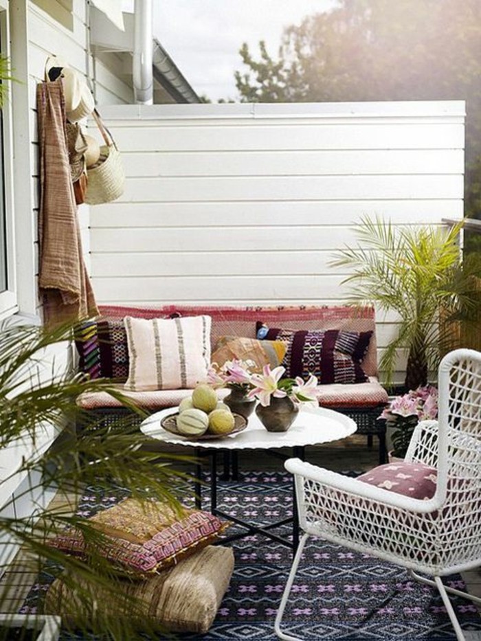 table basse ronde et chaise blanche en rotin petit canapé décoré de coussins, coussins d assise, brise vue bois blanchi, tapis noir à motifs orientaux