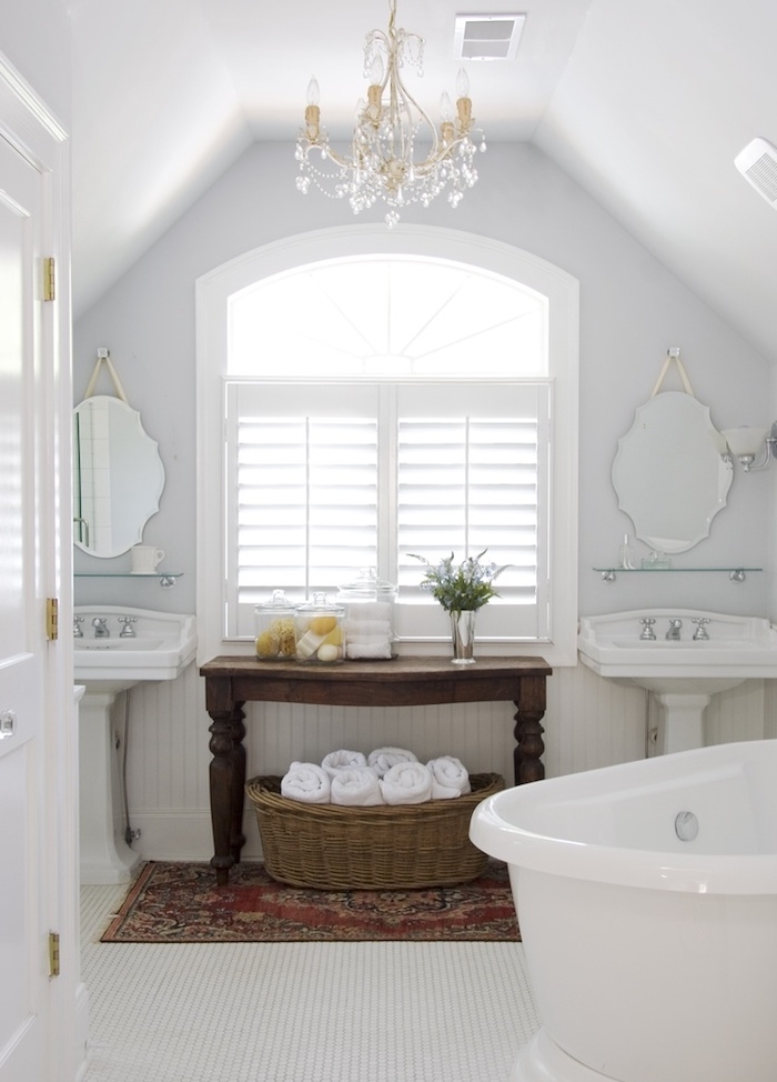 salle de bain blanche traditionnelle avec tapis oriental, petite table bois marron, baignoire blanche, miroirs vintage, lustre élégant